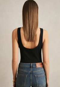 Must mustriba tank top avaraga lahtise tagumise osaga, kombineeritud keskmise pesu denim pükstega, millel on nahklogo pliit ja tagataskud.