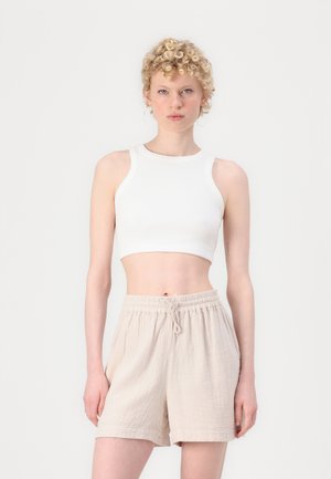White ribbed crop top with a high neckline paired with beige, loose-fitting shorts featuring an elastic waistband and drawstring detail.