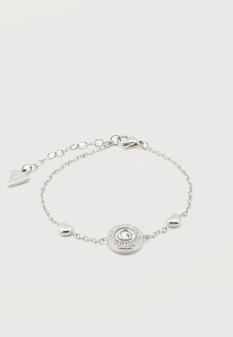 Ασημένιο βραχιόλι αλυσίδας με δύο φυλαχτά σε σχήμα καρδιάς, ένα στρογγυλό φυλαχτό με κρύσταλλα και λογότυπο 'G', και μια τριγωνική ετικέτα μάρκας σε μια αλυσίδα επέκτασης.