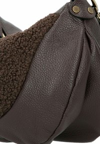 Bruine leren tas met een getextureerde bruine vachtaccent. Heeft een ronde vorm, zichtbare stitching en decoratieve hardware.