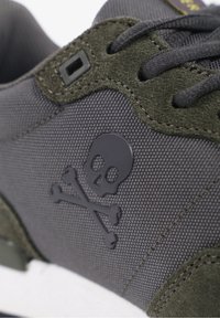Baskets gris foncé avec un dessus en tissu texturé, des accents en daim vert et un logo de crâne et os croisés noir sur le côté.
