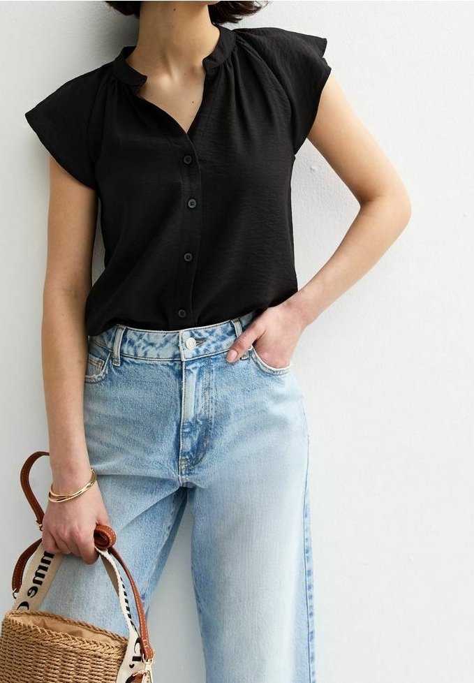 Blouse noire à manches courtes avec un devant boutonné et un col froncé, associée à un jean taille haute bleu clair et un sac en osier.
