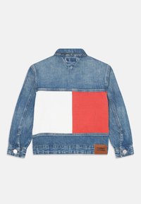 Veste en denim avec un délavage bleu clair, un bloc blanc et rouge au dos, et une étiquette en cuir brun avec la marque "TOMMY HILFIGER".