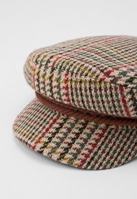 Vevd houndstooth-cap i beige, grønn, rød og brun, med en flettet brun bånd og en strukturert, rund form.