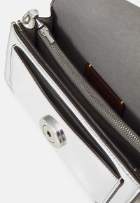 Portafoglio in metallo argentato con scomparto con cerniera e chiusura a bottone automatico. L'interno presenta una fodera in tessuto scuro e uno scomparto per carte.