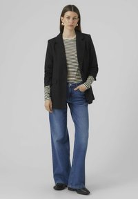 Blazer noir sur un haut à rayures à manches longues, associé à un jean bleu à jambes larges. Le tissu semble tissé, avec un design minimaliste et sans motifs.