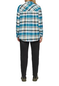 Camicia a scacchi con un motivo blu, nero e bianco, colletto a bottoni, maniche lunghe e orlo curvo. Abbinata a pantaloni e scarpe neri.