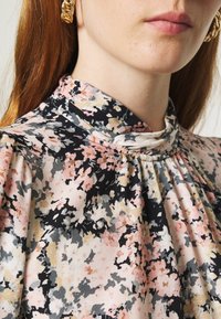 Blusa floreale con collo alto, caratterizzata da un motivo rosa chiaro, nero e grigio, realizzata in un tessuto testurizzato con dettagli arricciati.