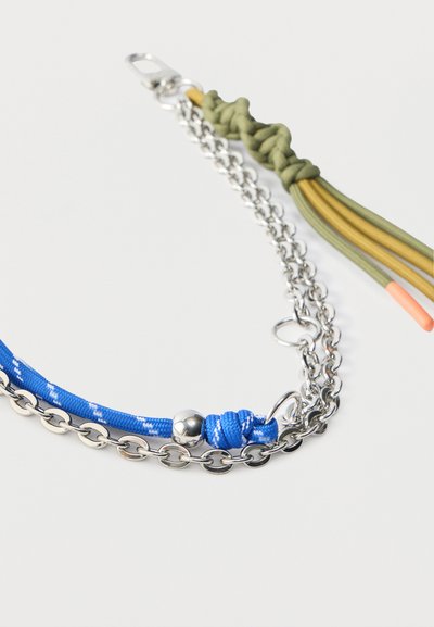 Αξεσουάρ από μέταλλο και πλεγμένο κορδόνι σε μπλε και πράσινο, με αλυσίδες από ασημί μέταλλο και πολύχρωμα φούντες. Περιλαμβάνει εξαρτήματα για στερέωση.
