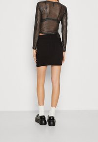 Svart stickad topp med långa ärmar har en genomskinlig, texturerad design. Matchad med en svart kjol som framhäver en figurnära silhuett och fickor.