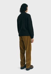 Suéter negro de punto trenzado con cuello redondo, combinado con pantalones de pana dorados. Presenta patrones texturizados y un corte holgado, visible desde la parte de atrás.