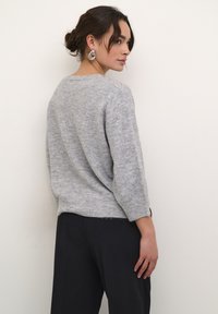 Lichtgrijze gebreide trui met driekwart mouwen en een relaxte pasvorm, gecombineerd met donkere wijde broekspijpen. Gelaagd textiel en minimale details.
