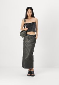 Top nero senza spalline con texture arricciata, abbinato a una lunga gonna di jeans grigia. La modella porta una borsa verde e indossa sandali neri.