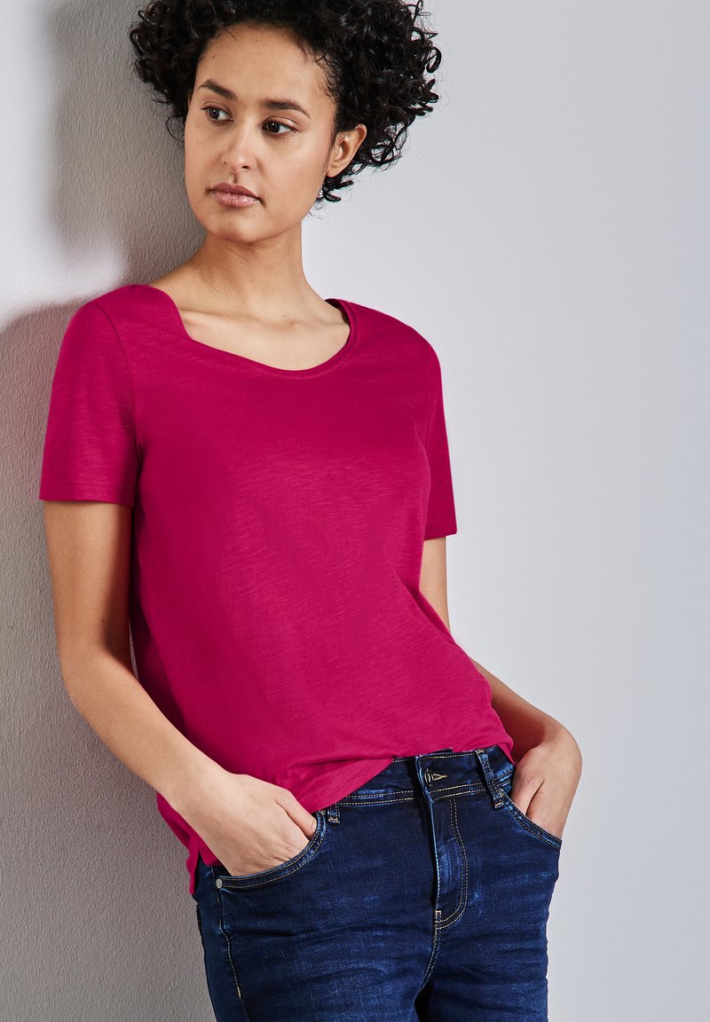 T-shirt fucsia a maniche corte con scollatura a girocollo, indossato infilato in jeans blu scuro. Tessuto morbido con una superficie liscia. Senza fantasie.