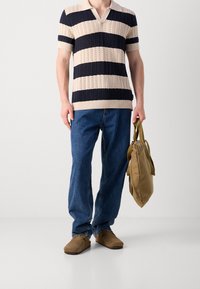 Pletené polo tričko v béžových a námořnicky modrých pruzích, doplněné modrými džínami a hnědými nazouvacími botami. V ruce drží hnědou plátěnou tašku.