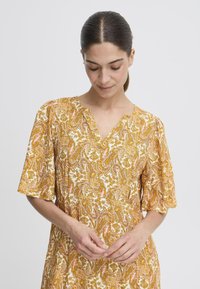 Rochie cu model paisley în galben și alb, cu decolteu în V, mâneci scurte și material moale. Detalii notabile includ desene florale complexe.