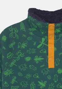 Camicetta verde a maniche lunghe con motivi di insetti, dotata di un colletto morbido blu navy e una placca per i bottoni arancione brillante, realizzata in tessuto morbido.