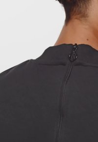 Čierny športový top s vysokým výstrihom, vybavený krátkym zipsom na zadnej strane a hladkou textúrou. Viditeľné sú detaily švov.