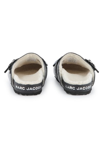 Scarpe slip-on nere con una morbida fodera interna bianca e una suola testurizzata, caratterizzate da una fibbia argentata e dal marchio "Marc Jacobs" sul tallone.