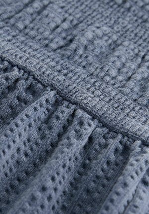 Mintázott kék kötött anyag kiemelkedő mintákkal és redőkkel, sima vízszintes csíkkal. Az anyag lágy és könnyűnek tűnik.