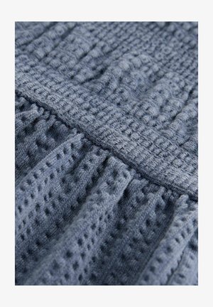 Tissu en tricot bleu texturé avec des motifs en relief et des plis, présentant une bande horizontale lisse. Le matériau semble doux et léger.