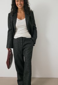 Zwarte textuur pak met bloemmotief, op maat gemaakte blazer met uitlopende mouwen, gecombineerd met losse broek en een kastanjebruine gevlochten handtas.