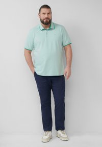Lichtgroen poloshirt met donkergroene accenten, gecombineerd met marineblauwe broek. De outfit heeft een casual ontwerp en een relaxte pasvorm. Witte sneakers maken de look compleet.