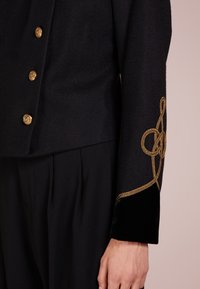 Černá vlněná bunda s zlatými knoflíky, složitou zlatou výšivkou na rukávu a černými sametovými prvky na manžetě.