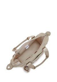 Bolso beige con dos asas cortas, cremallera abierta que muestra un interior vacío con un pequeño bolsillo y etiqueta del logo de Kipling en el interior.