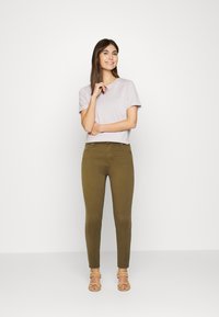 Jeans skinny verde-azeitona combinados com uma t-shirt lilás clara. O conjunto apresenta um design simples, textura suave e hardware mínimo.