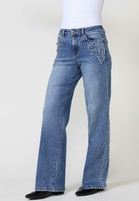 Jeans de mezclilla azul con un diseño de pierna recta, que cuentan con costuras decorativas en los bolsillos delanteros y un estilo clásico de cinco bolsillos.