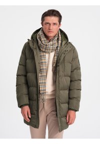 Olivengrøn puffjakke med hætte og lynlås foran, med elastiske manchetter. Kombineret med et ternet tørklæde i beige og brune nuancer.