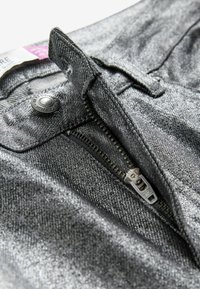 Kovově šedý denim se zapínáním na zip, stříbrnými doplňky a jemným texturovaným detailem. Detailní pohled na pas a otvor.
