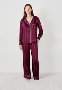 Bordowy komplet piżamowy uszyty z miękkiego materiału, z białymi pionowymi paskami, koszulą zapinaną na guziki z kieszonką oraz spodniami o szerokich nogawkach.