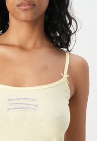 Yellow ribbed tank top with thin straps and bow accents; features a blue fish graphic design on the front. Soft, stretchy fabric.