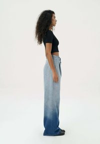 Lichtblauwe denim wijde broekspijpen, met een ombre-gradiënt naar een donkerder blauw, met een hoge taille en zijzakken. Zwarte aangesloten top gedragen.