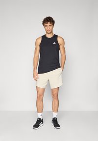 Débardeur sans manches noir, shorts beige clair, chaussures de sport noires, chaussettes blanches avec trois bandes et accents de logo.