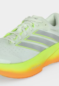 Λευκό και γκρι αθλητικό παπούτσι Adidas με σόλα σε διαβάθμιση νέον κίτρινου και πορτοκαλί, γκρι ρίγες και λευκά κορδόνια.