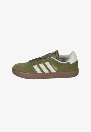 Zapatilla deportiva de ante verde oliva con suela marrón, tira blanca en el talón, cordones y tres rayas blancas laterales.