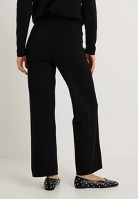 Pantalons larges tricotés noirs avec une texture douce, associés à des chaussures plates noires ornées de clous en métal argenté sur le bout.