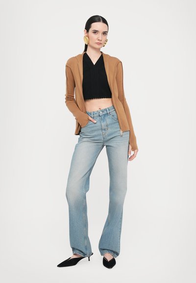 Hnědý zip-up cardigan, černý crop top, modré džíny s vysokým pasem a černé lodičky na jehlovém podpatku na postavě proti jednoduchému bílému pozadí.