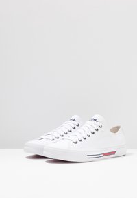 Paar flacher weißer Segeltuch-Sneaker mit weißen Schnürsenkeln, Gummisohlen und roten und blauen Streifen an der Seite.