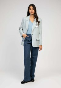 Blazer rayé en bleu clair et blanc avec un patch "A", associé à un pantalon large à rayures marines, et des chaussures noires. Texture plate.