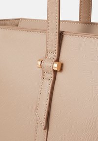 Sac fourre-tout synthétique beige avec surface texturée, présentant un design épuré, des poignées fines et des éléments décoratifs dorés.