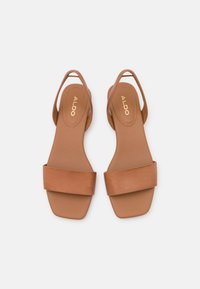 Sandali in pelle color cuoio con punta quadrata, ampia fascia frontale e design slingback. Texture liscia con un logo discreto sulla soletta.