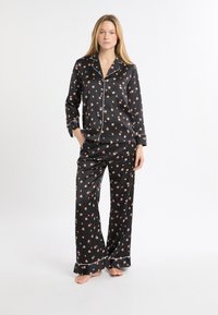 Czarny zestaw piżamowy w kwiaty, składający się z koszuli na guziki z długim rękawem ozdobionej białą lamówką oraz pasujących luźnych spodni z falbaną na dole.
