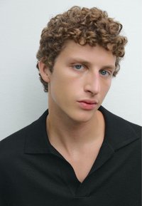 Svart polo tröja med V-formad krage, åtsittande design och korta ärmar. Lockigt hår och ljus hy. Mjuk, slät textur.