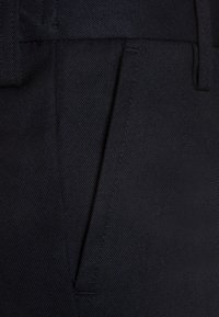 Pantalons noirs en tissu texturé, avec une coupe flatteuse à l'avant, des poches latérales et un design ajusté, mettant en avant des lignes nettes et des bords propres.