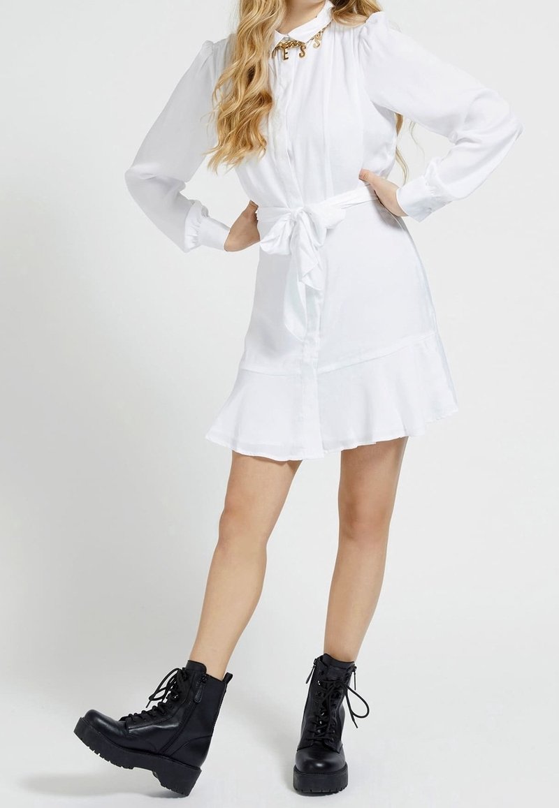 Weißes langärmliges Kleid mit Knopfverschluss, Gürtelbindung in der Taille, ausgestelltem Saum, kombiniert mit schwarzen Kampfstiefeln mit dicken Sohlen.
