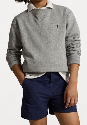 Suéter gris de algodón con cuello redondo y puños acanalados, superpuesto sobre una camisa blanca con cuello; combinado con pantalones cortos azul marino.